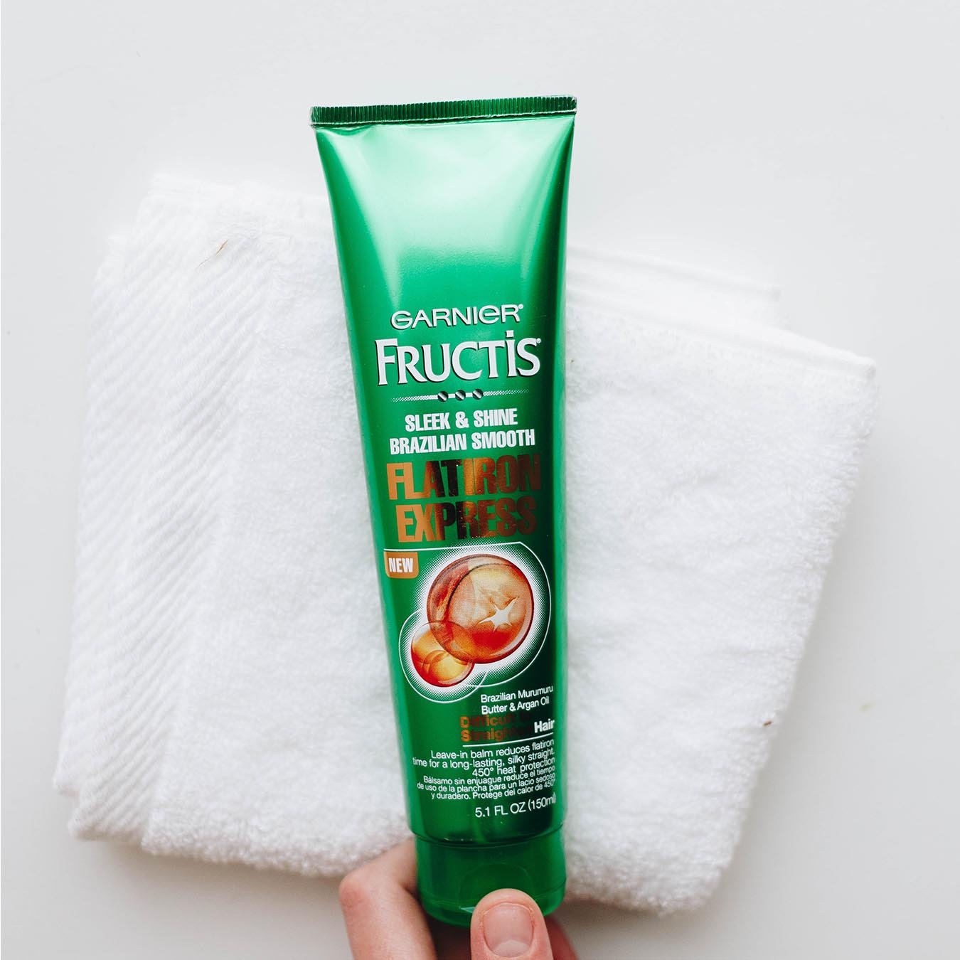Garnier Fructis Sleek & Shine Flatiron Express being held over white hand towels on a white background.